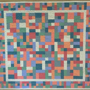 Op de afbeelding: Een wit quilt met een patchwork-ontwerp met vierkanten in verschillende kleuren, waaronder rood, oranje, groen, blauw en paars. Het quilt is afgewerkt met een witte rand.