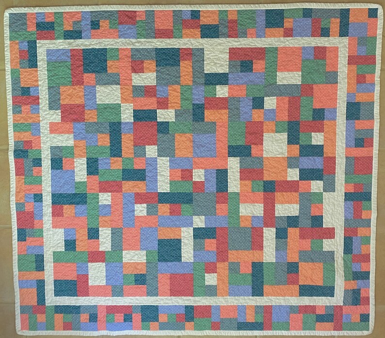 Op de afbeelding: Een wit quilt met een patchwork-ontwerp met vierkanten in verschillende kleuren, waaronder rood, oranje, groen, blauw en paars. Het quilt is afgewerkt met een witte rand.