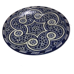 May include: A large, round ceramic plate with a blue and white geometric pattern. The plate has a decorative border and a central design featuring a repeating motif of stylised swirls and circles.