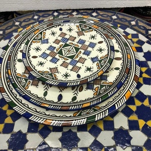 Peut inclure: Un ensemble de trois assiettes en céramique avec des motifs géométriques complexes dans des tons de bleu, vert, marron et orange. Les assiettes sont empilées les unes sur les autres, la plus petite étant en haut.