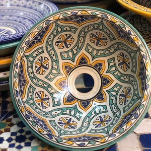 May include: A ceramic bowl with a blue, green and yellow geometric pattern. The bowl is round and has a small hole in the centre.
