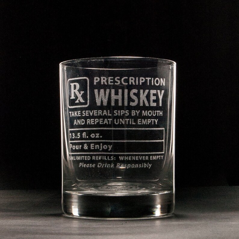 Op de afbeelding: Een helder glazen whiskeyglas met een gegraveerd ontwerp met de tekst "Prescription Whiskey". Het glas heeft een label met de tekst "Neem meerdere slokjes door de mond en herhaal tot het leeg is". Het staat ook "13,5 fl. oz. Giet & Geniet" en "Onbeperkt bijvullen: wanneer leeg. Drink verantwoord."