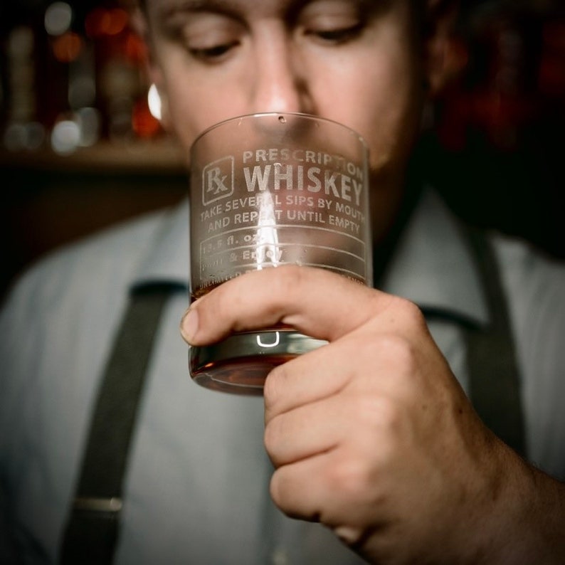 Op de afbeelding: Een helder glas met de tekst "Prescription Whiskey" gegraveerd aan de zijkant. De tekst luidt "Neem meerdere slokjes door de mond en herhaal tot het glas leeg is."