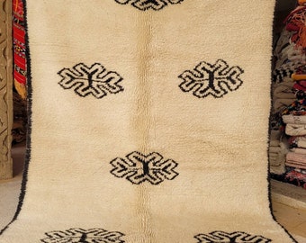 Könnte beinhalten: Ein weißer Wollteppich mit einem schwarzen geometrischen Muster. Der Teppich hat einen Fransenrand und ist in Marokko hergestellt.