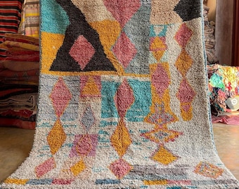 May include: A colorful Moroccan rug with a geometric pattern in shades of blue, pink, yellow, and white. The rug has a fringe border and is made of wool.