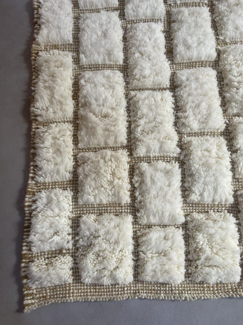 May include: A white and beige woven rug with a checkered pattern. The rug is made of fluffy, textured yarn.