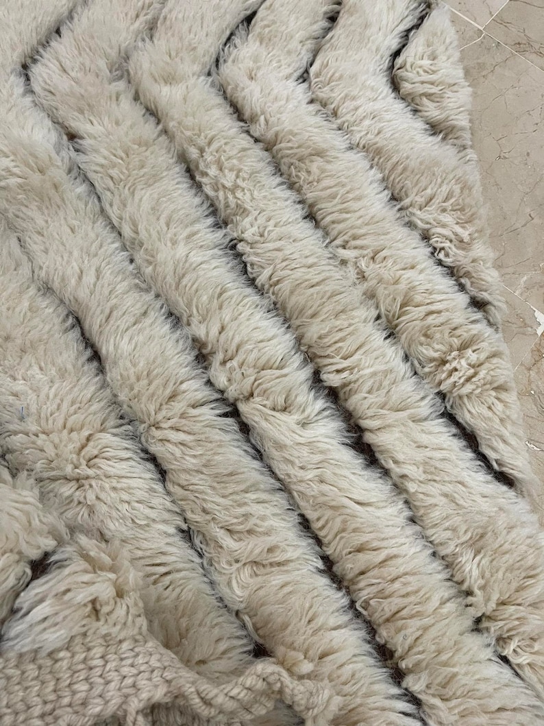 K&ouml;nnte beinhalten: Ein wei&szlig;er, flauschiger Teppich mit einem Chevron-Muster. Der Teppich ist aus Wolle und hat eine weiche, pl&uuml;schige Textur.