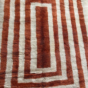 May include: A white and orange geometric patterned rug with a square design. The rug has a thick, plush texture.