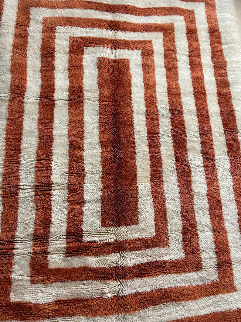 May include: A white and orange geometric patterned rug with a square design. The rug has a thick, plush texture.