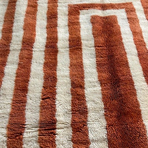 May include: A close-up of a brown and white striped rug with a geometric pattern. The rug is made of a soft, fluffy material.