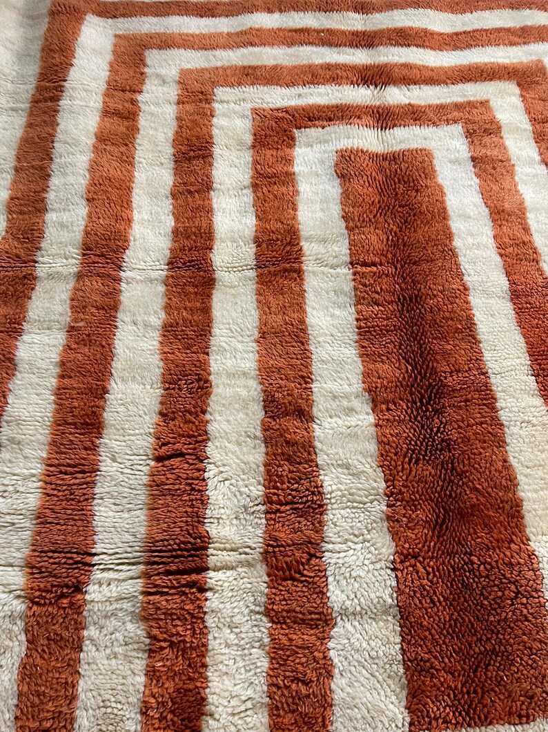 May include: A close-up of a brown and white striped rug with a geometric pattern. The rug is made of a soft, fluffy material.