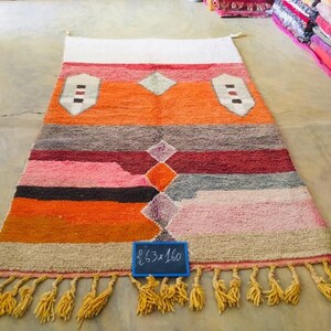 May include: A colorful Moroccan rug with a geometric pattern in shades of orange, pink, red, and gray. The rug has a fringe border and a handwritten sign that reads "2.63 x 1.60".