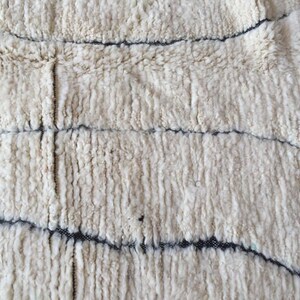 May include: White fluffy rug with a woven pattern of black lines. The rug has a soft, textured surface.