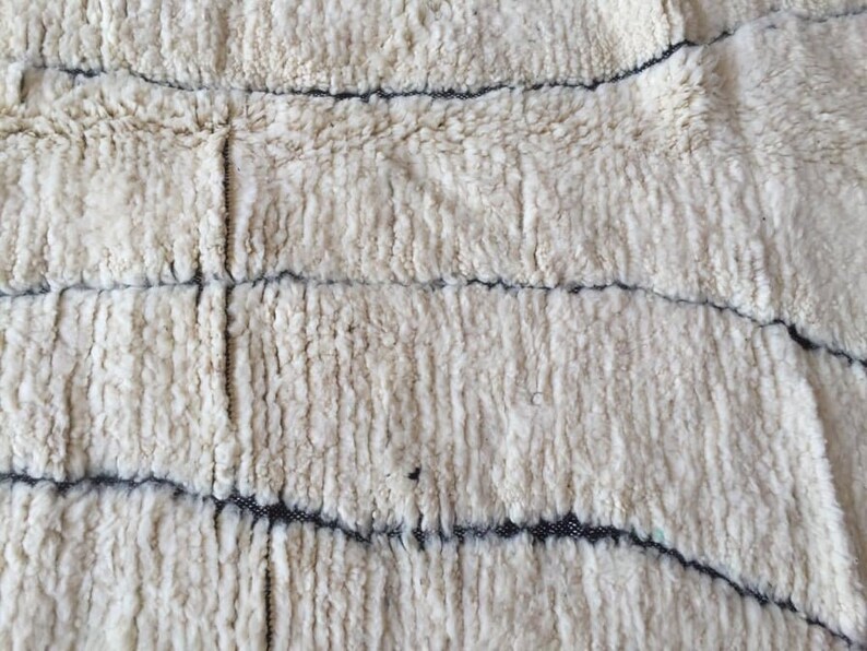 May include: White fluffy rug with a woven pattern of black lines. The rug has a soft, textured surface.