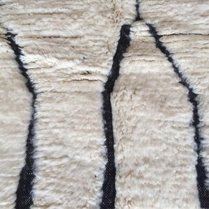 May include: Close-up of a white rug with a black geometric pattern. The rug has a soft, fluffy texture.
