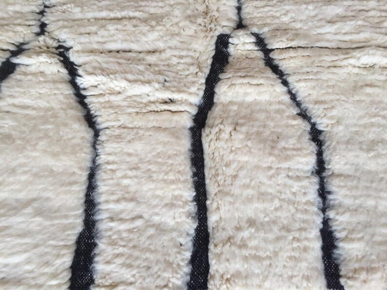 May include: Close-up of a white rug with a black geometric pattern. The rug has a soft, fluffy texture.