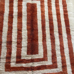 May include: A white and brown rug with a geometric pattern of concentric squares. The rug has a shaggy texture.