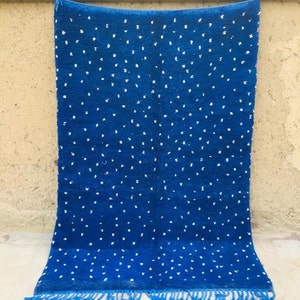 May include: A blue and white rug with a repeating pattern of white dots on a blue background. The rug has fringe on the bottom edge.