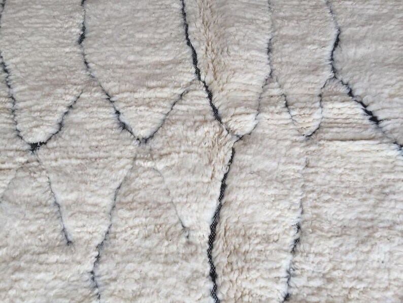 May include: A white rug with a geometric pattern in black. The rug has a soft, fluffy texture.