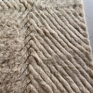 May include: A cream-colored fluffy rug with a chevron pattern. The rug has a soft, plush texture and is made of a high-quality material.