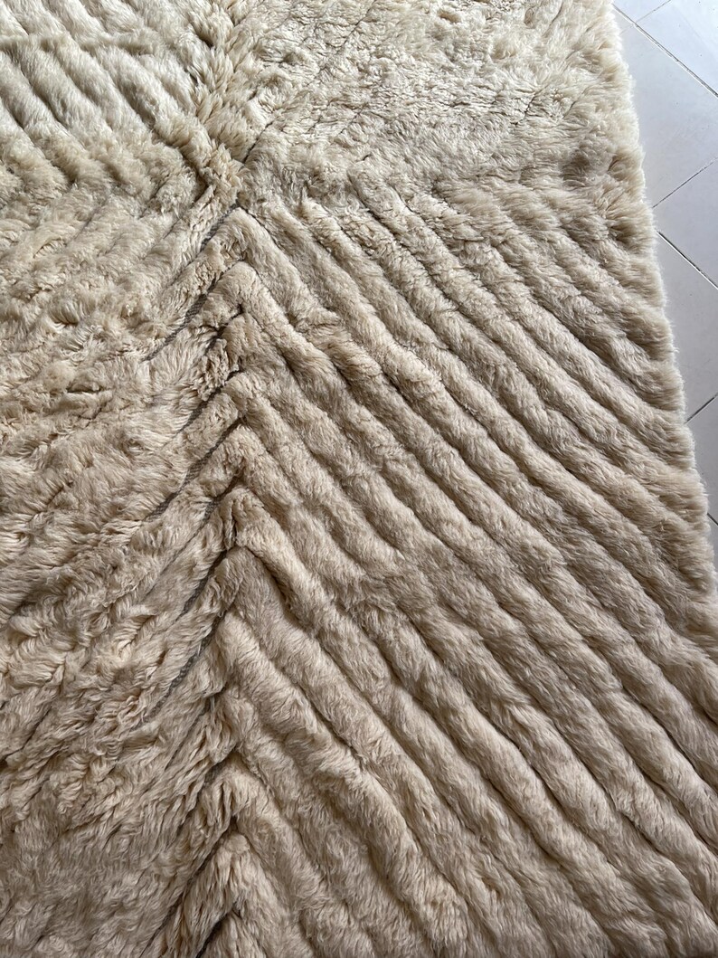 May include: A cream-colored fluffy rug with a chevron pattern. The rug has a soft, plush texture and is made of a high-quality material.