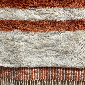 May include: A white and orange striped rug with a fringe border. The rug is made of a soft, fluffy material.