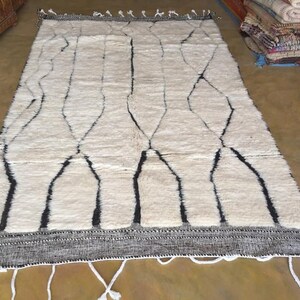 May include: A white and black Moroccan rug with a geometric pattern. The rug has a fringe border and is made of wool.