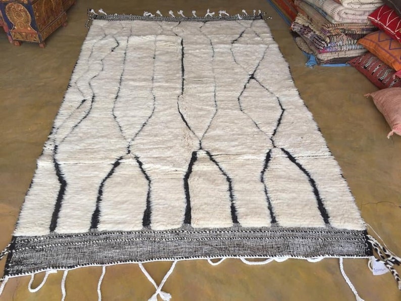 May include: A white and black Moroccan rug with a geometric pattern. The rug has a fringe border and is made of wool.