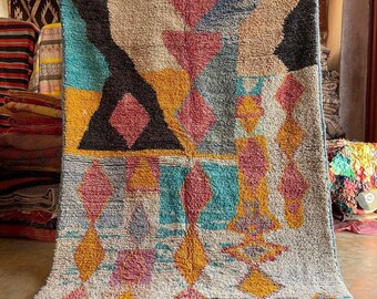 May include: A colorful Moroccan rug with a geometric pattern in shades of blue, pink, yellow, and white. The rug has a fringe border and is made of wool.