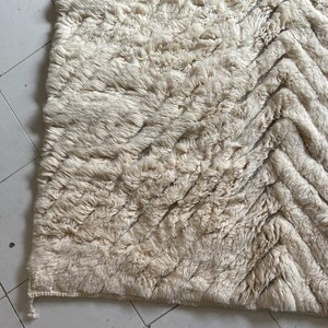 May include: A cream-colored rug with a chevron pattern. The rug is made of a soft, fluffy material.
