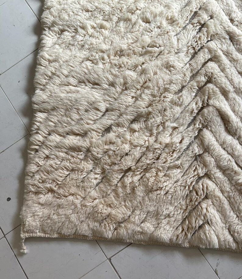 May include: A cream-colored rug with a chevron pattern. The rug is made of a soft, fluffy material.