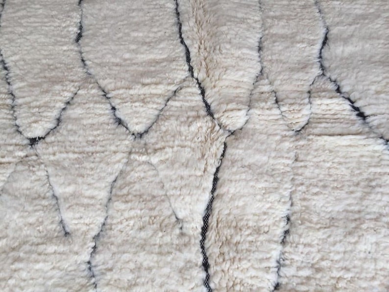 May include: A white rug with a geometric pattern in black. The rug has a soft, fluffy texture.