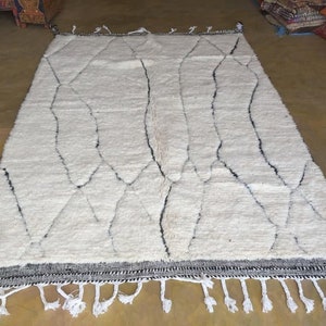May include: White Moroccan rug with a geometric pattern in black. The rug has a fringe border.
