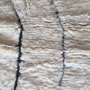 May include: Close-up of a white, fluffy, woven textile with black stitching. The texture is soft and plush, resembling a sheepskin rug.