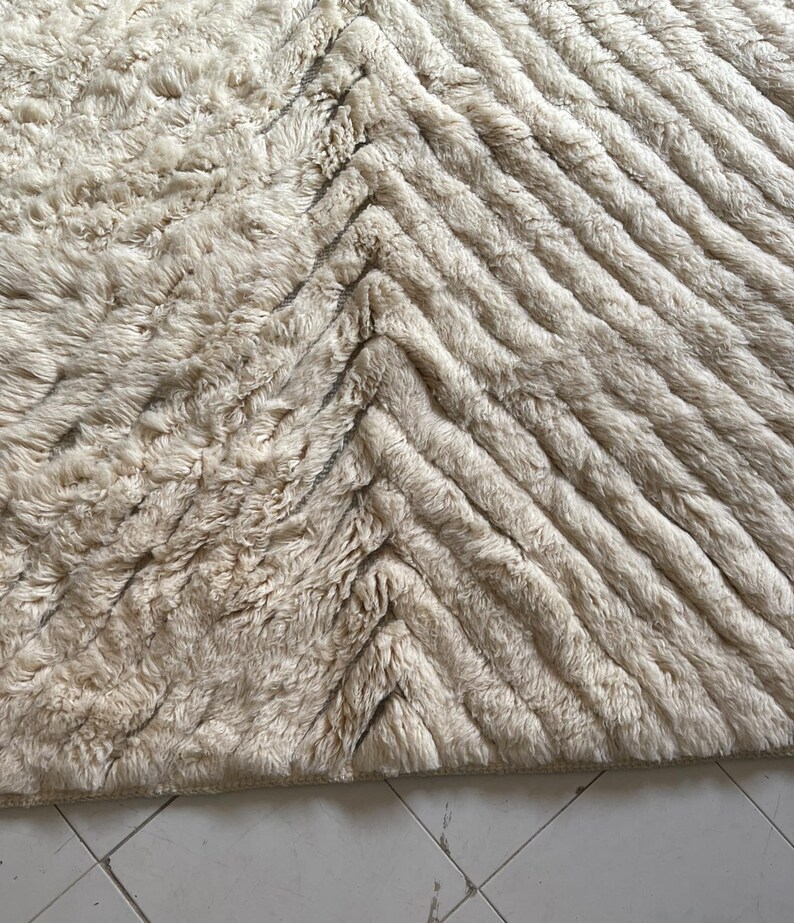 May include: A cream-colored rug with a chevron pattern. The rug is made of a soft, fluffy material.