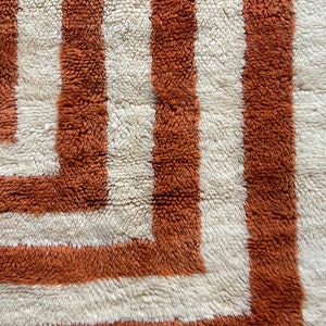 May include: Close-up of a white and orange shag rug with a geometric pattern. The rug has a thick pile and a soft texture.