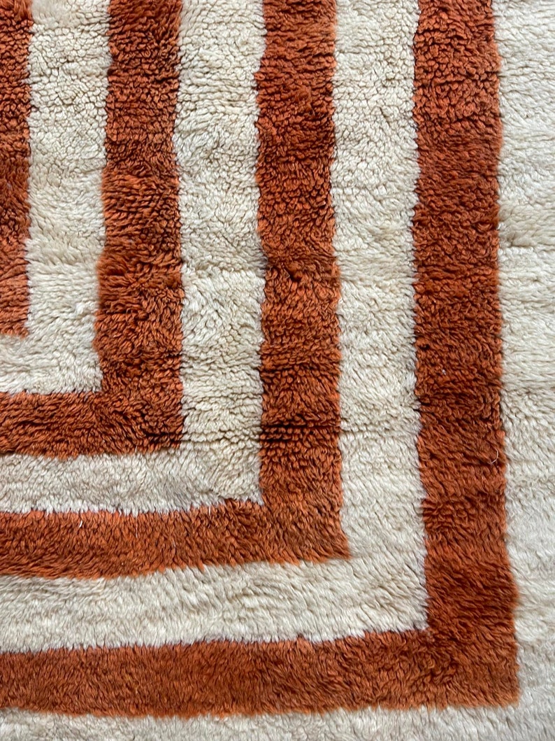 May include: Close-up of a white and orange shag rug with a geometric pattern. The rug has a thick pile and a soft texture.
