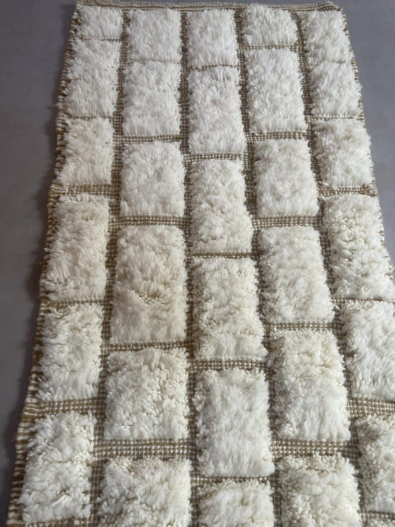 May include: White and beige rectangular rug with a tufted texture. The rug has a grid pattern with squares of white tufting and beige woven lines.