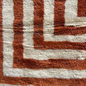 May include: A close-up of a brown and white striped rug with a geometric pattern. The rug is made of a soft, fluffy material.