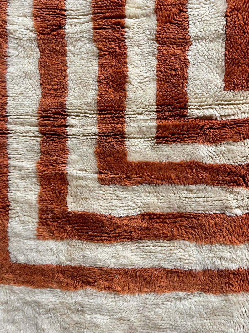 May include: A close-up of a brown and white striped rug with a geometric pattern. The rug is made of a soft, fluffy material.