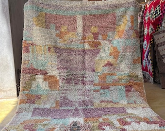 May include: A colorful Moroccan rug with a geometric pattern in shades of pink, orange, yellow, and blue. The rug has a fringe border and is made of wool.
