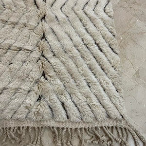 K&ouml;nnte beinhalten: Ein wei&szlig;er und brauner Teppich mit Muster und Fransenrand. Der Teppich hat eine weiche, flauschige Textur.