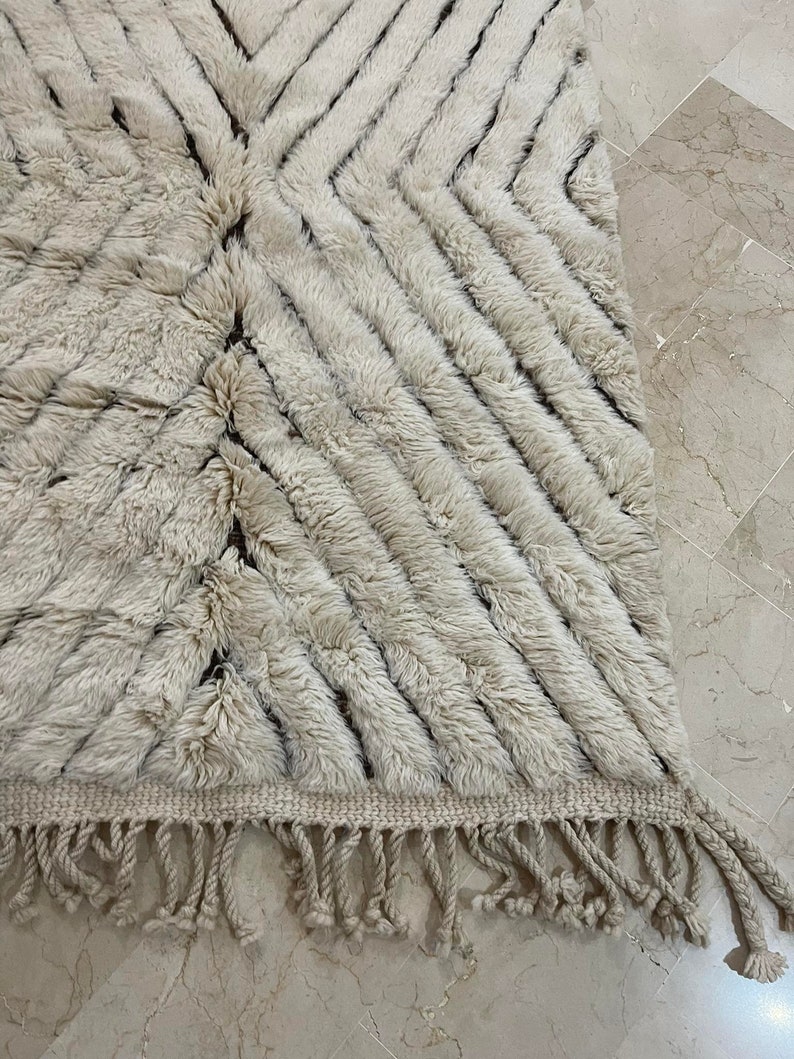 K&ouml;nnte beinhalten: Ein wei&szlig;er und brauner Teppich mit Muster und Fransenrand. Der Teppich hat eine weiche, flauschige Textur.