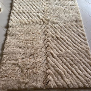 May include: A cream-colored, fluffy rug with a chevron pattern. The rug is made of a soft, plush material and has a subtle sheen.