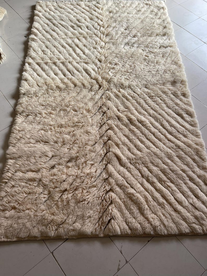 May include: A cream-colored, fluffy rug with a chevron pattern. The rug is made of a soft, plush material and has a subtle sheen.