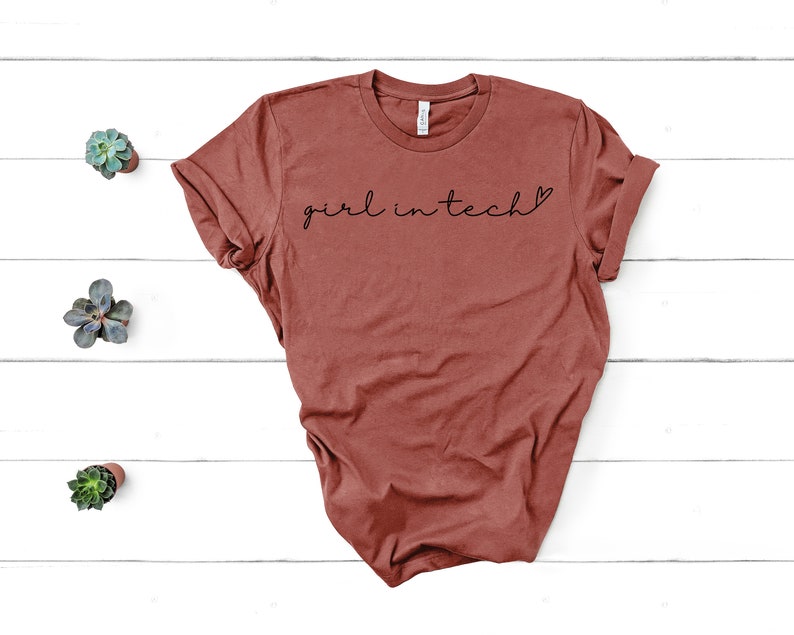 May include: A rust-colored t-shirt with the text "girl in tech" in black lettering with a small heart symbol.