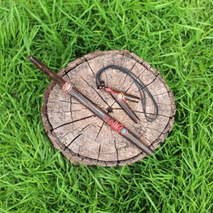 Op de afbeelding: Een houten rookpijp met gekleurde kralen en een bijpassende hanger aan een zwart koord. De pijp en de hanger liggen op een boomstronk.