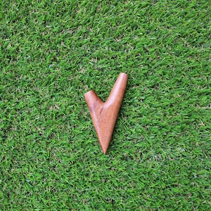 May include: A wooden pipe shaped like a V, with a smooth, brown finish. The pipe is sitting on a green grassy surface.