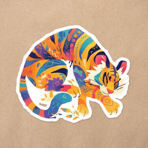 May include: A colorful illustration of a tiger with a patterned design. The tiger is curled up in a sleeping position with its head resting on its paws. The illustration is done in a vibrant style with bright colors and intricate details.