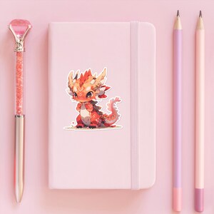 a pink notebook with a sticker of a baby dragon next to it